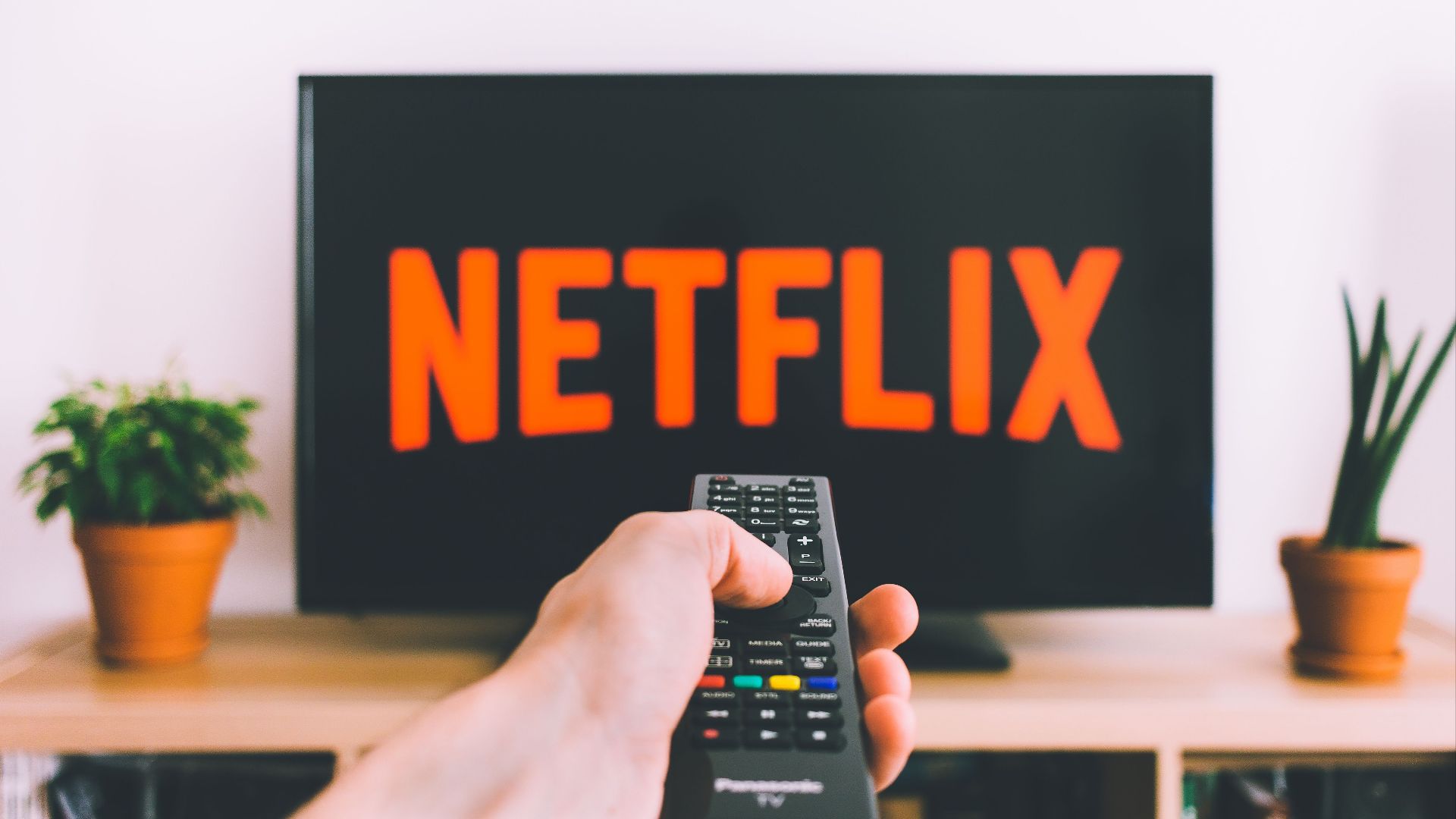 A hand holding a TV remote in front of a screen with Netflix, perfect for streaming and movie night themes.