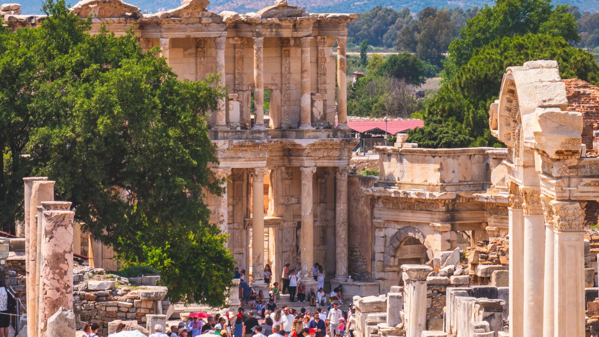 Tourists exploring ancient ruins at Ephesus, Türkiye under the summer sun.