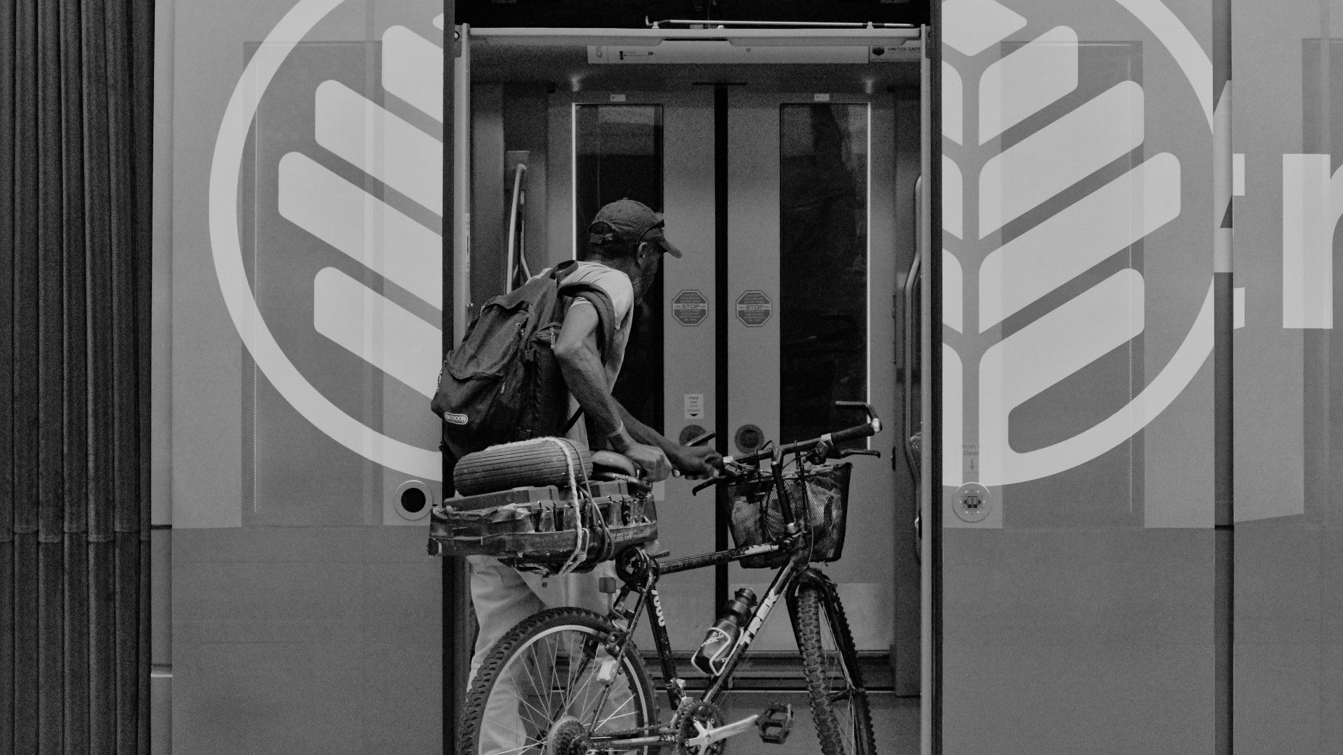 A cyclist with a backpack and bicycle entering a modern train station in an urban setting.