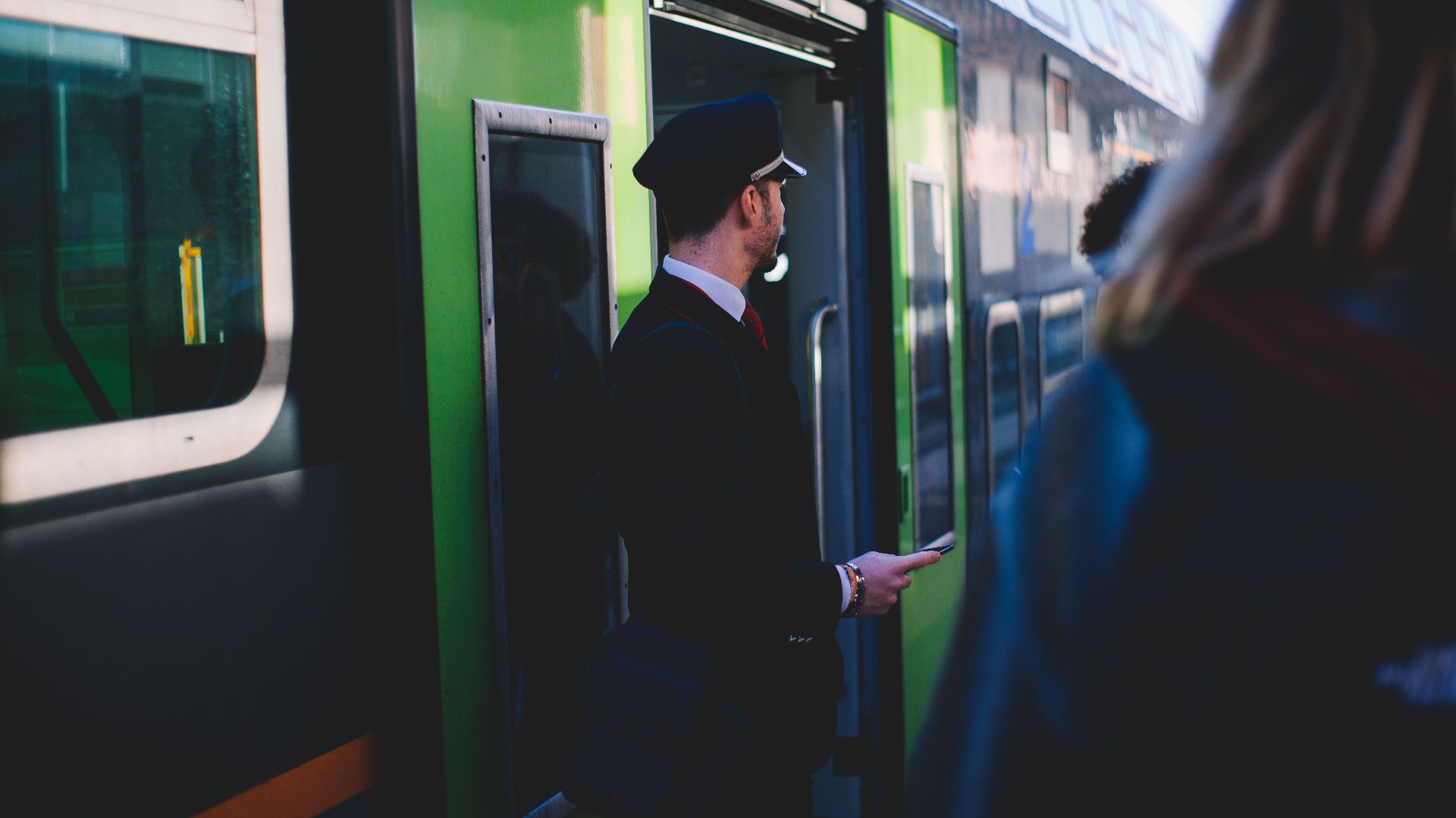 A train conductor at the entrance of a green train in Venice, Italy. Daytime scene with passengers.