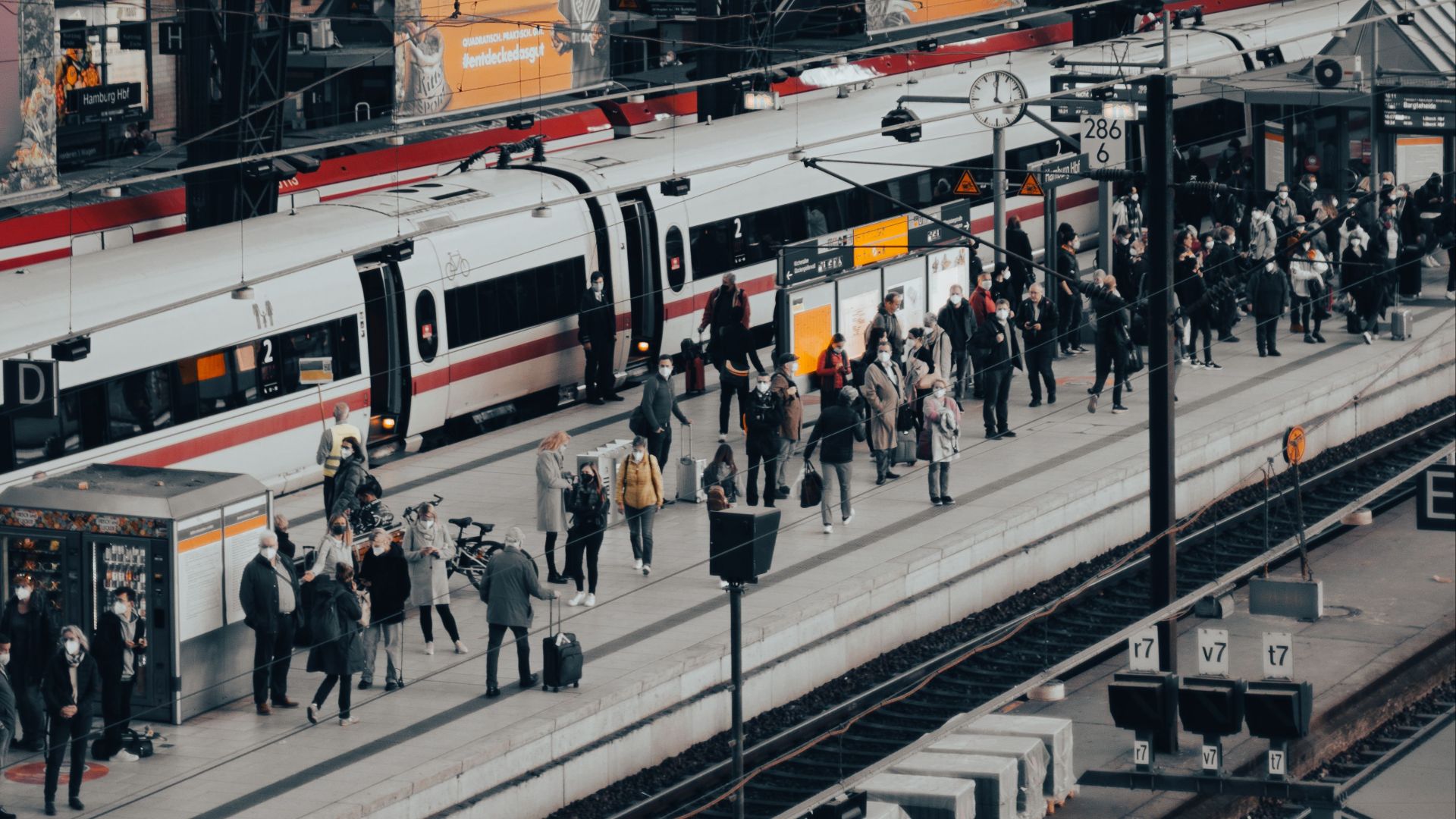 A bustling train station with commuters boarding and alighting trains under an arched roof.