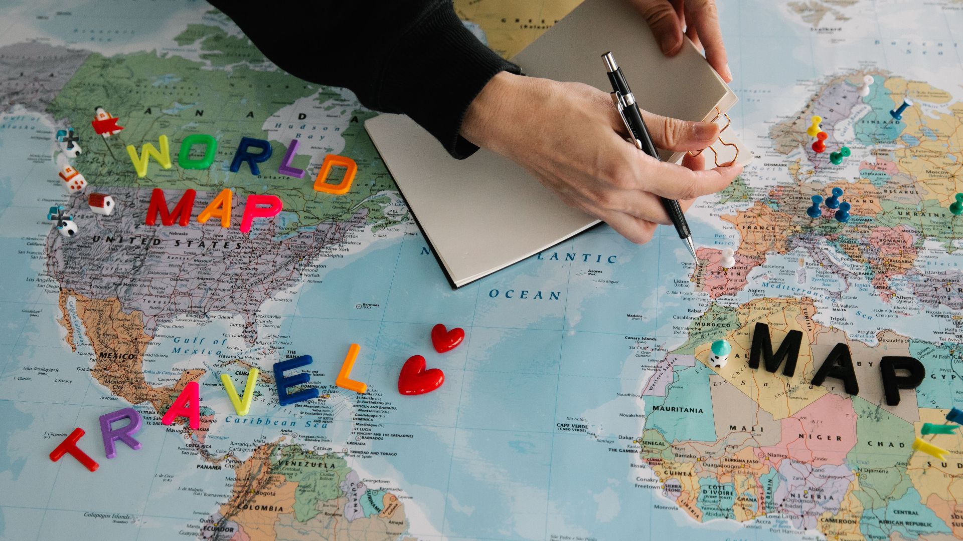 Hands holding pen and notebook over vibrant world map planning a journey.