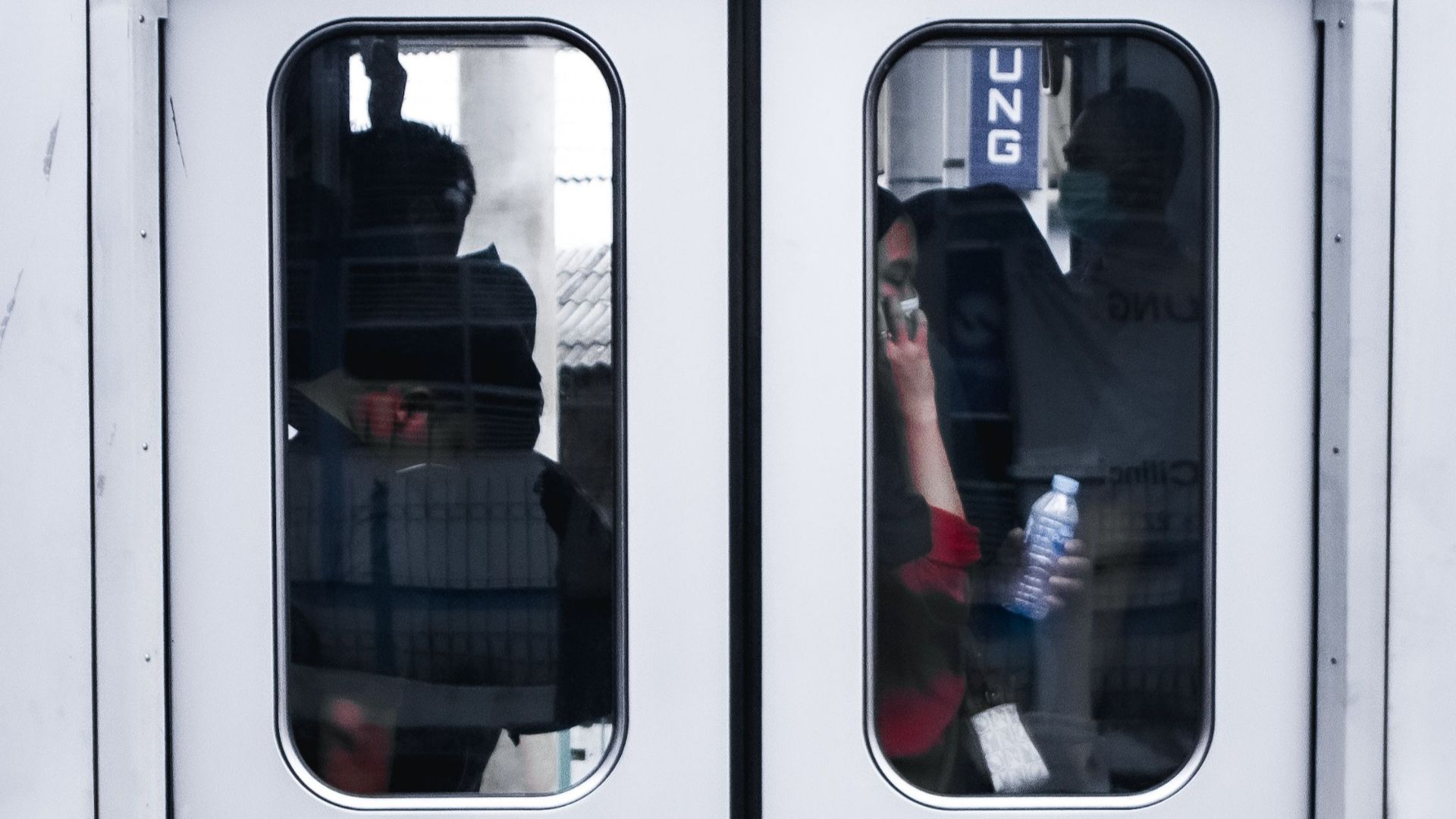 Vertical shot of a train door with reflections showing passengers.