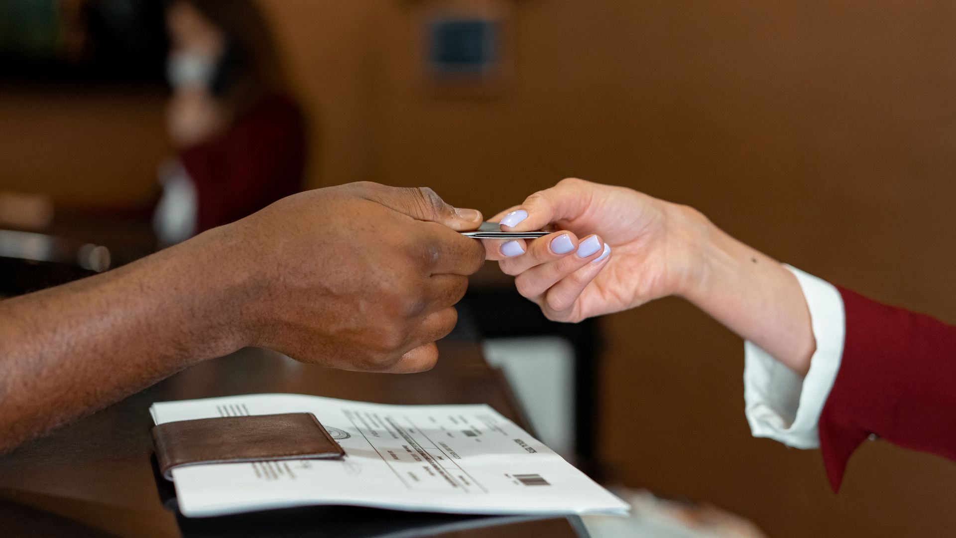 Close-up of a hotel receptionist receiving a credit card from a guest, highlighting a transaction at check-in.
