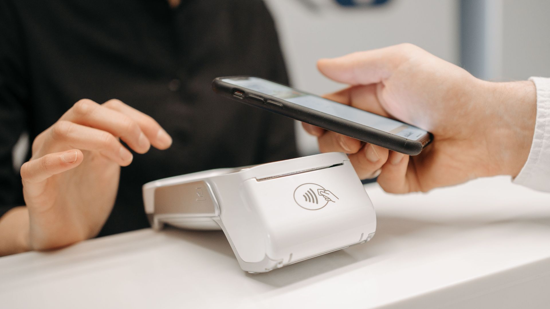 Person using a smartphone for contactless payment at a retail counter, highlighting cashless convenience.