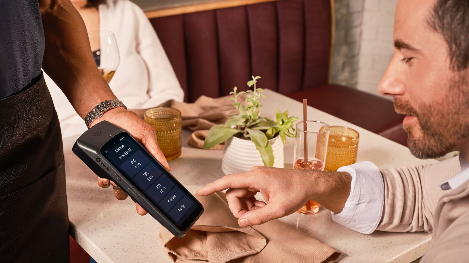 A diner uses a handheld POS system for digital tipping in a casual restaurant setting.