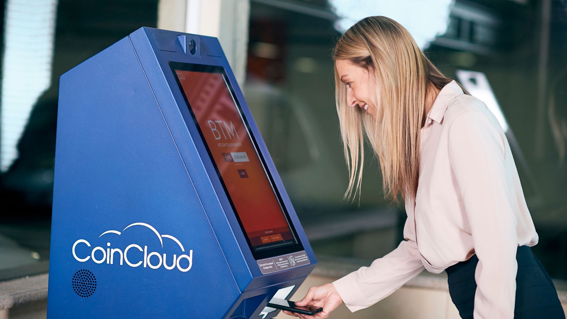 Woman smiling while using a CoinCloud cryptocurrency ATM indoors.