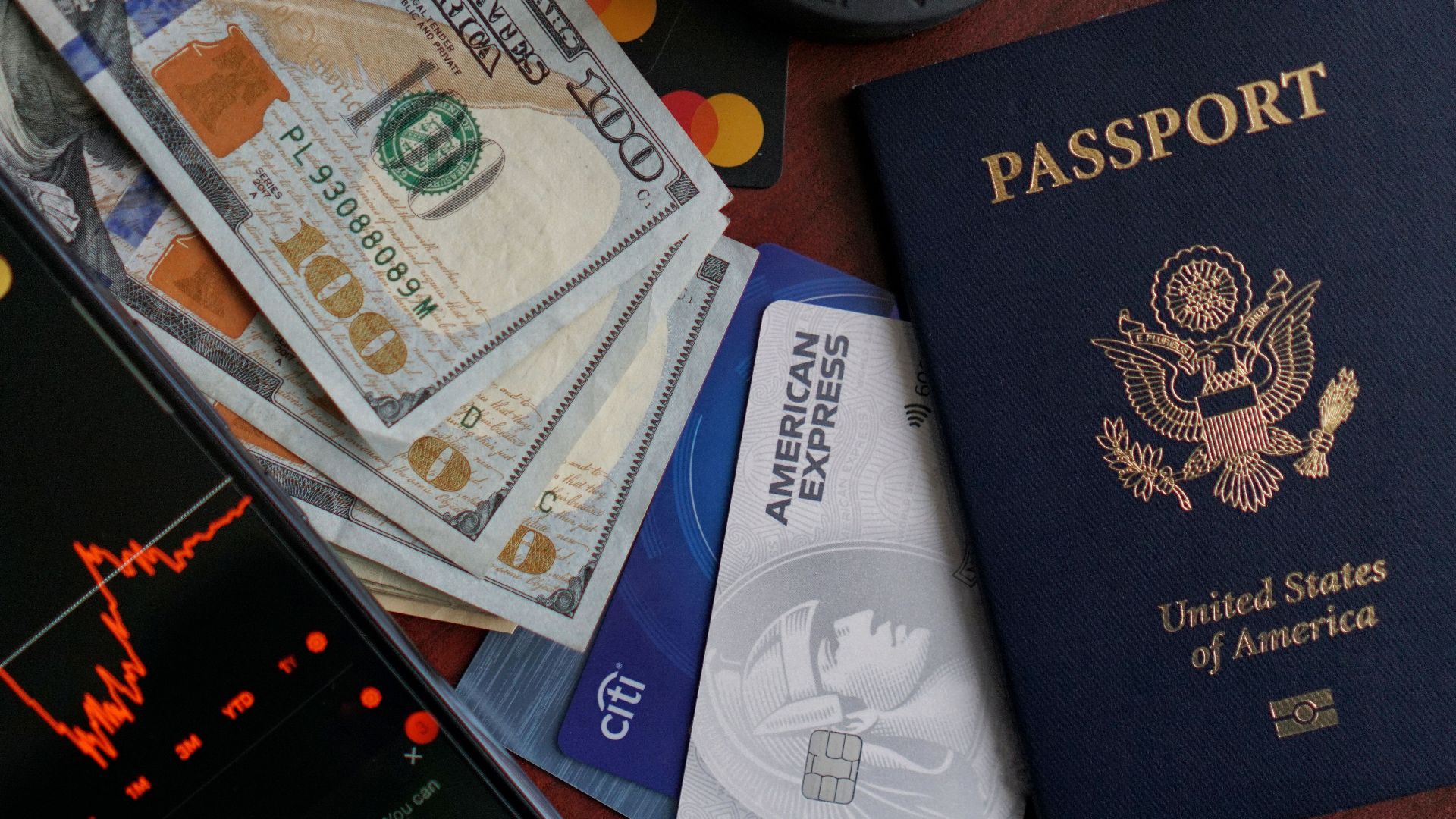 Top view of US passport, credit cards, cash, and phone showing financial graph, ideal for travel themes.