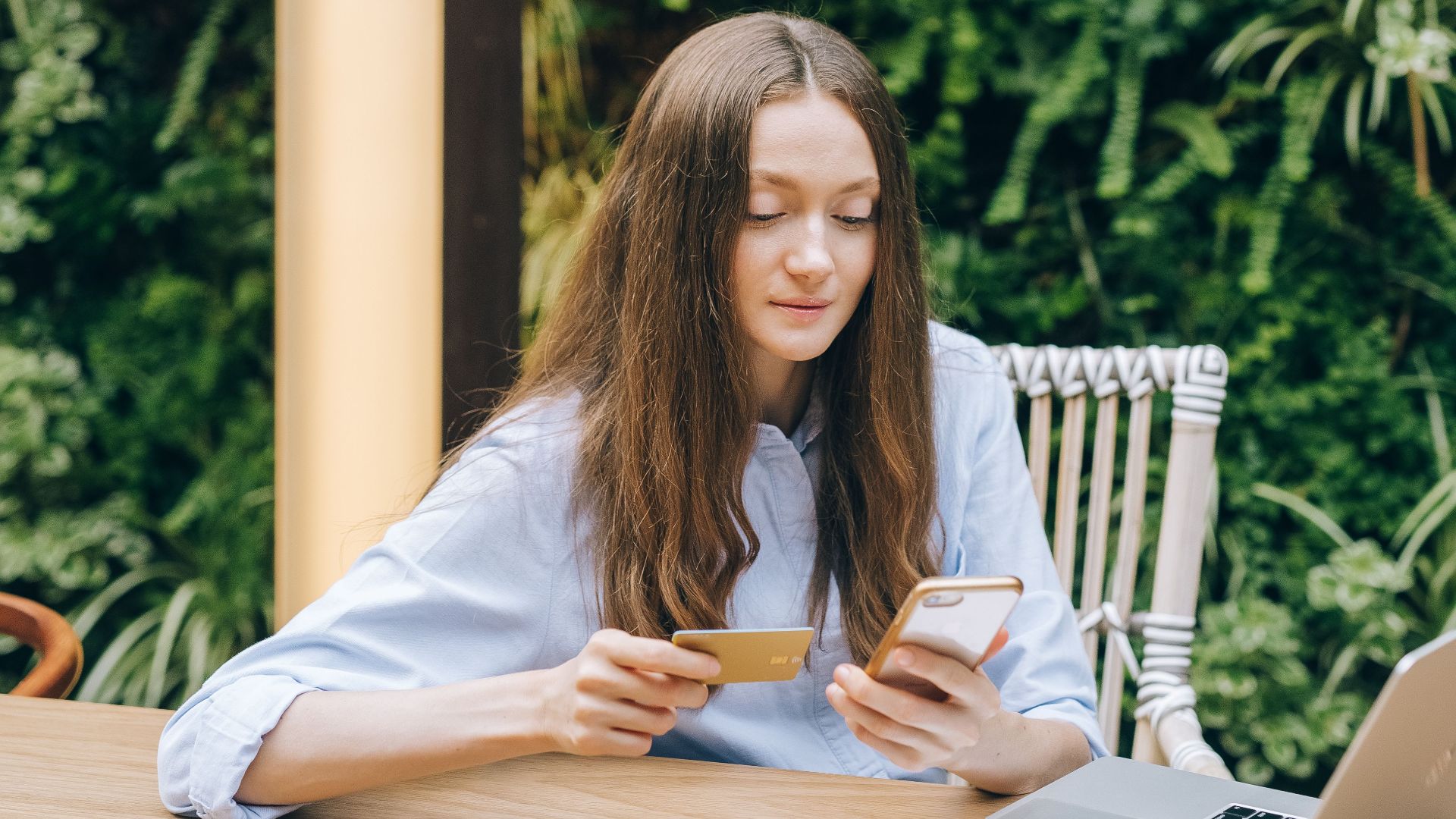Young woman using smartphone and credit card for online shopping outdoors.