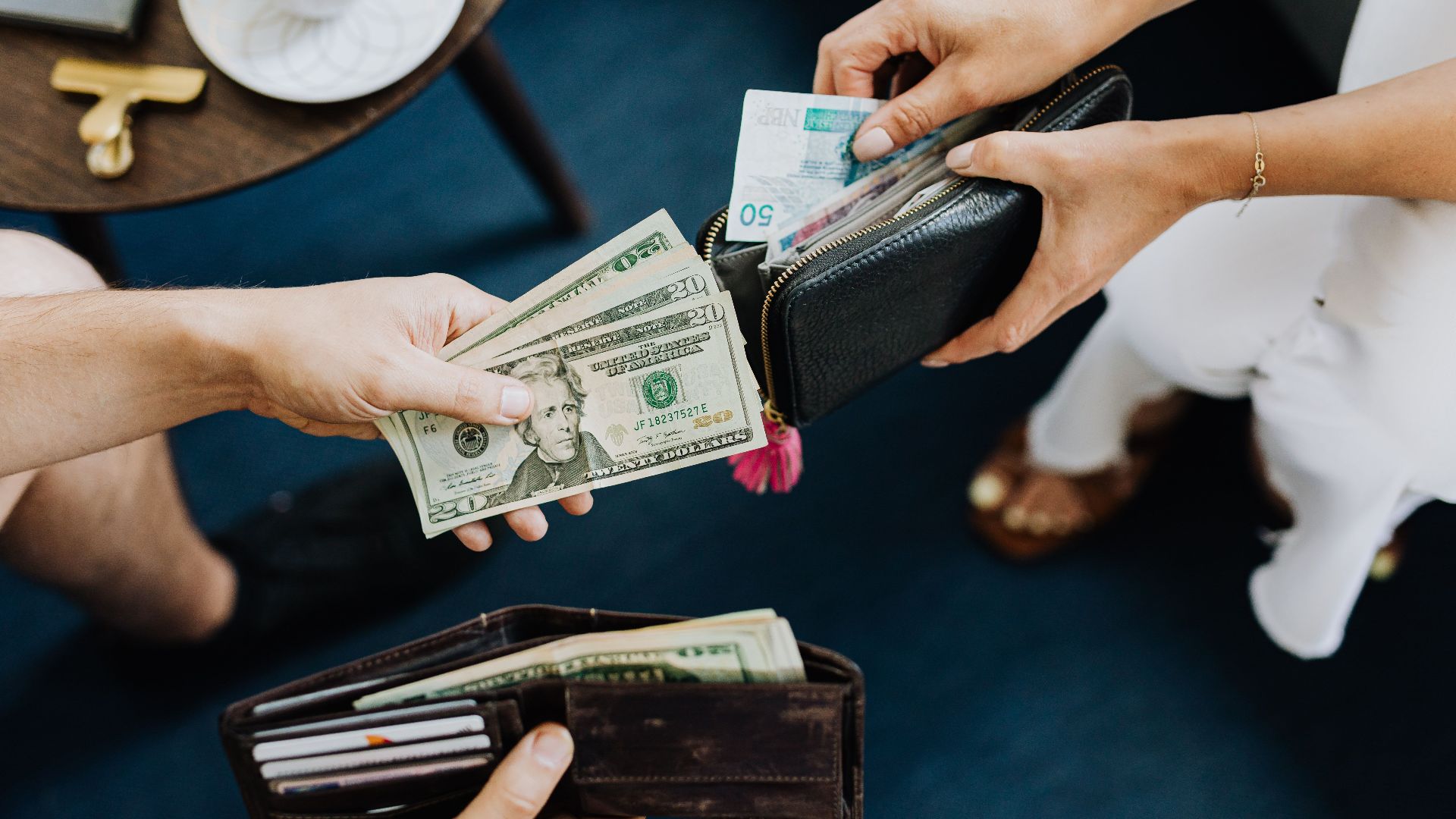 Close-up of two people exchanging US dollars and currency with wallets on a table.