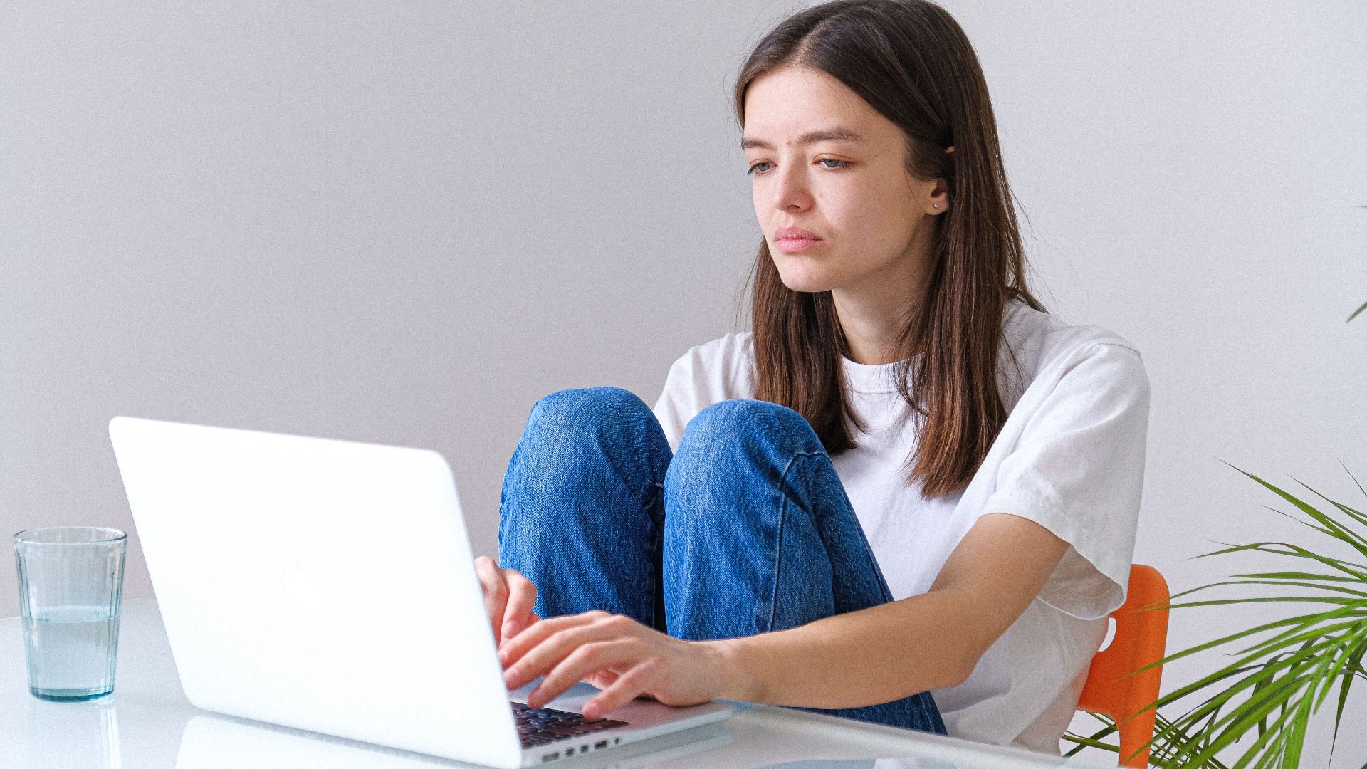 Young woman in casual clothes focused on laptop in a home office setting.