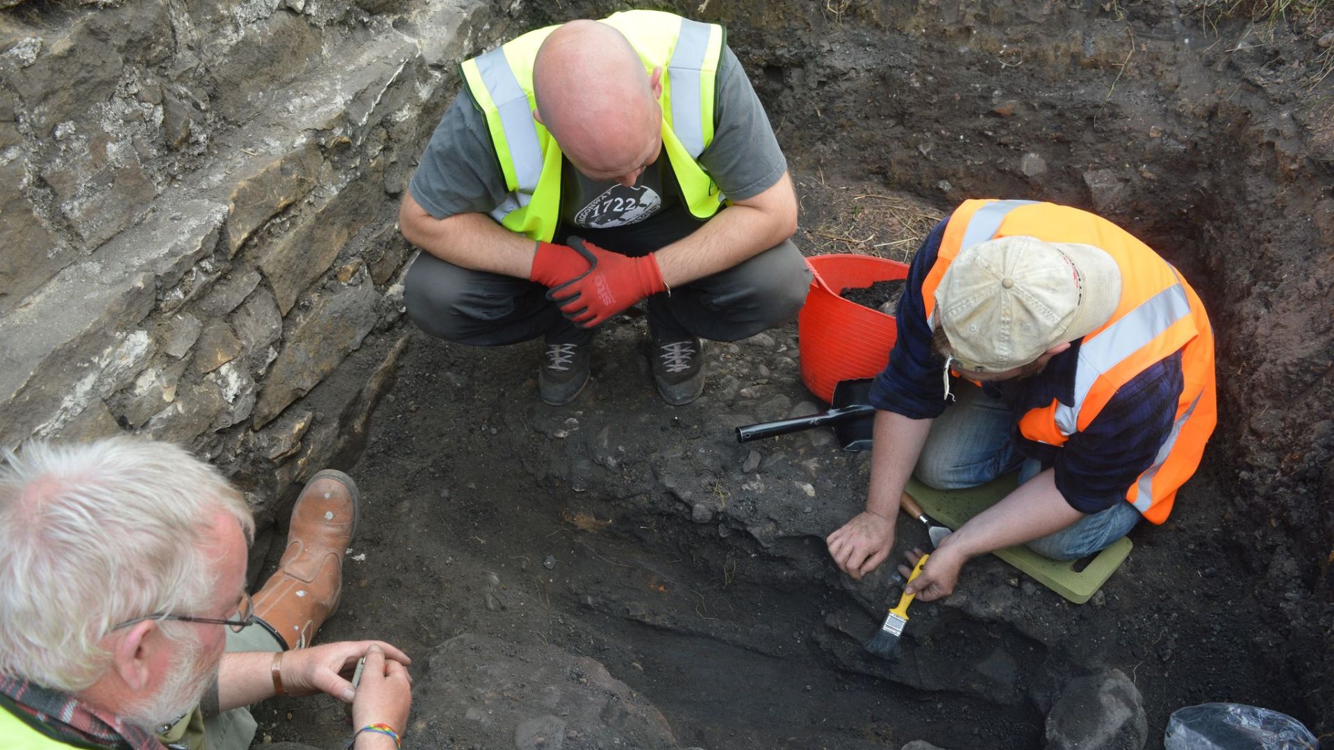 Three individuals crouching around a feature in the process of excavating it.