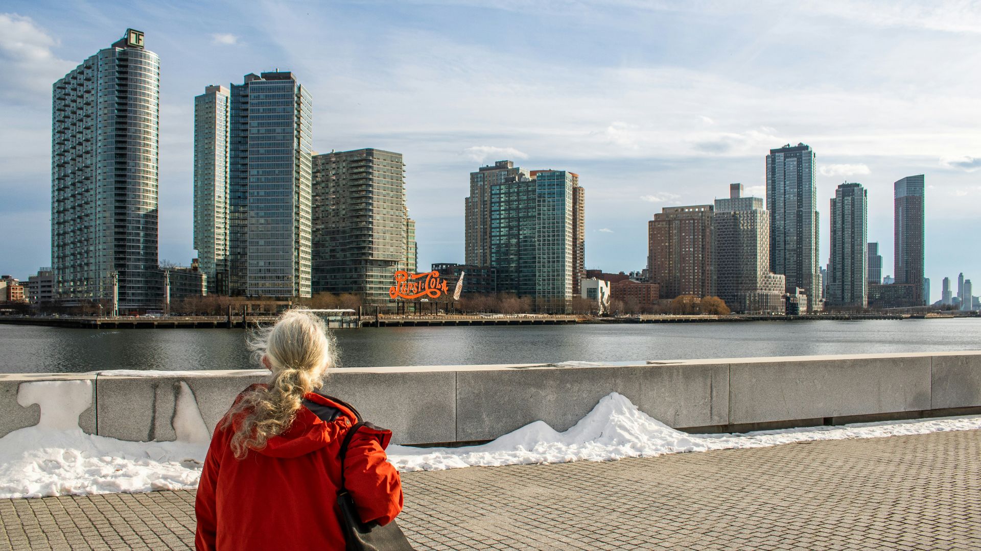 Woman in red jacket facing city skyline across water