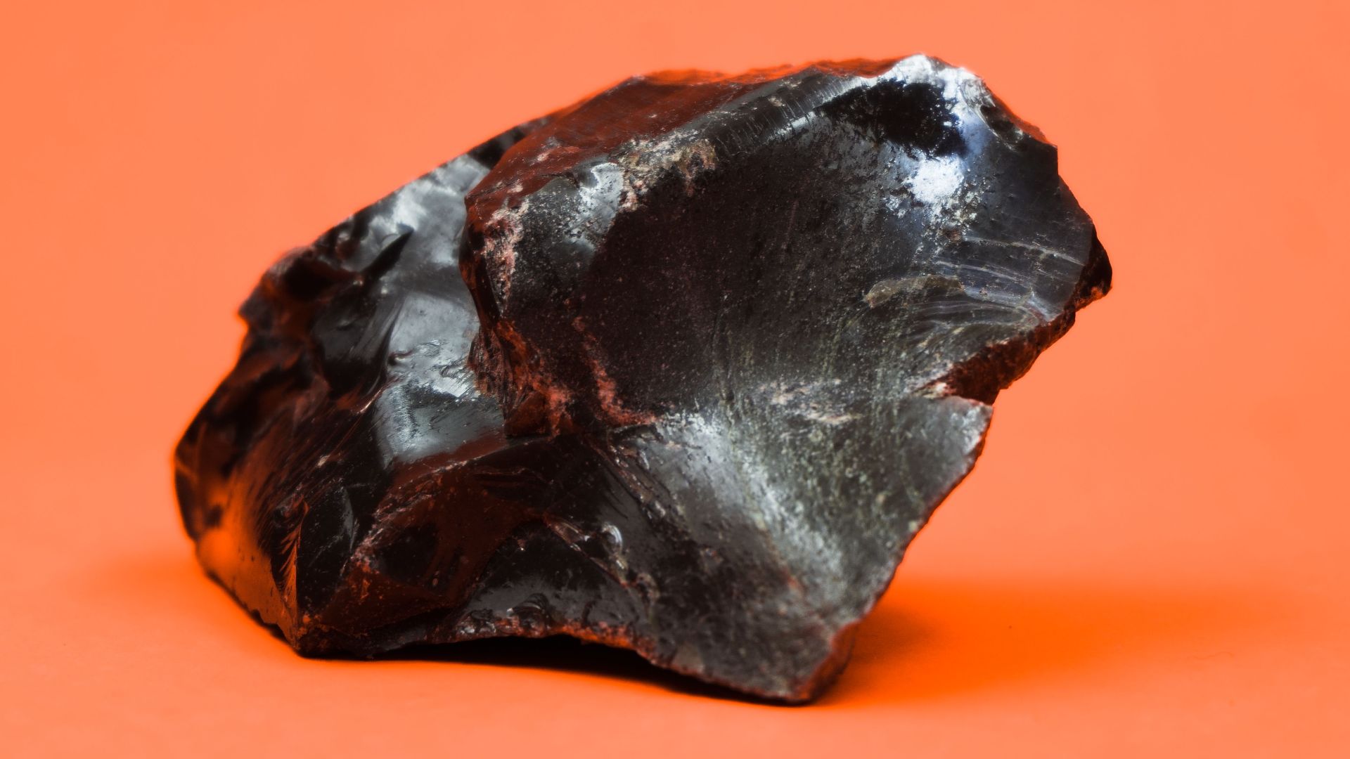 Close-up shot of a glossy obsidian stone with a sharp texture against a vibrant orange background.