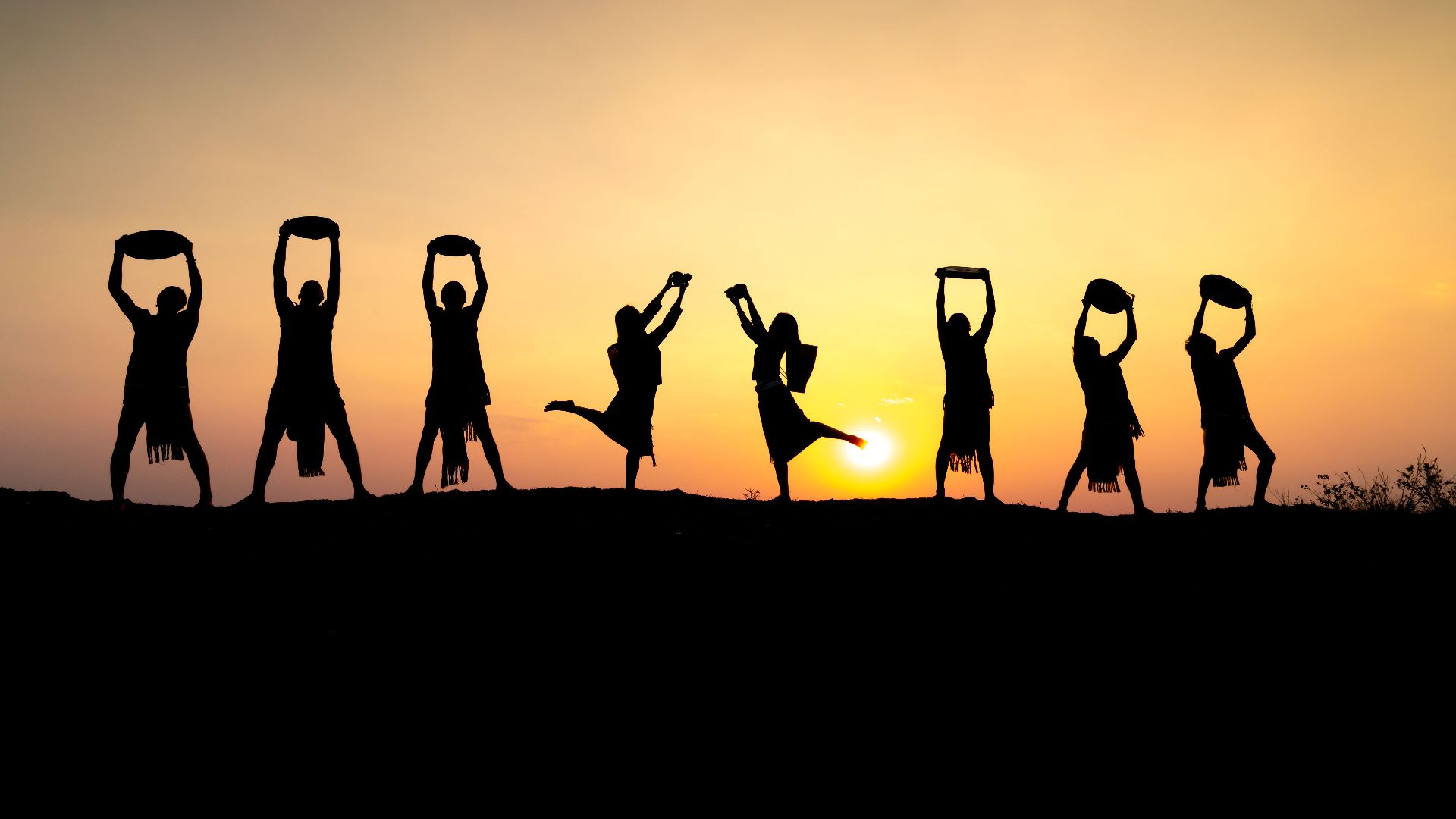 Group silhouetted against a sunset during a traditional dance performance.