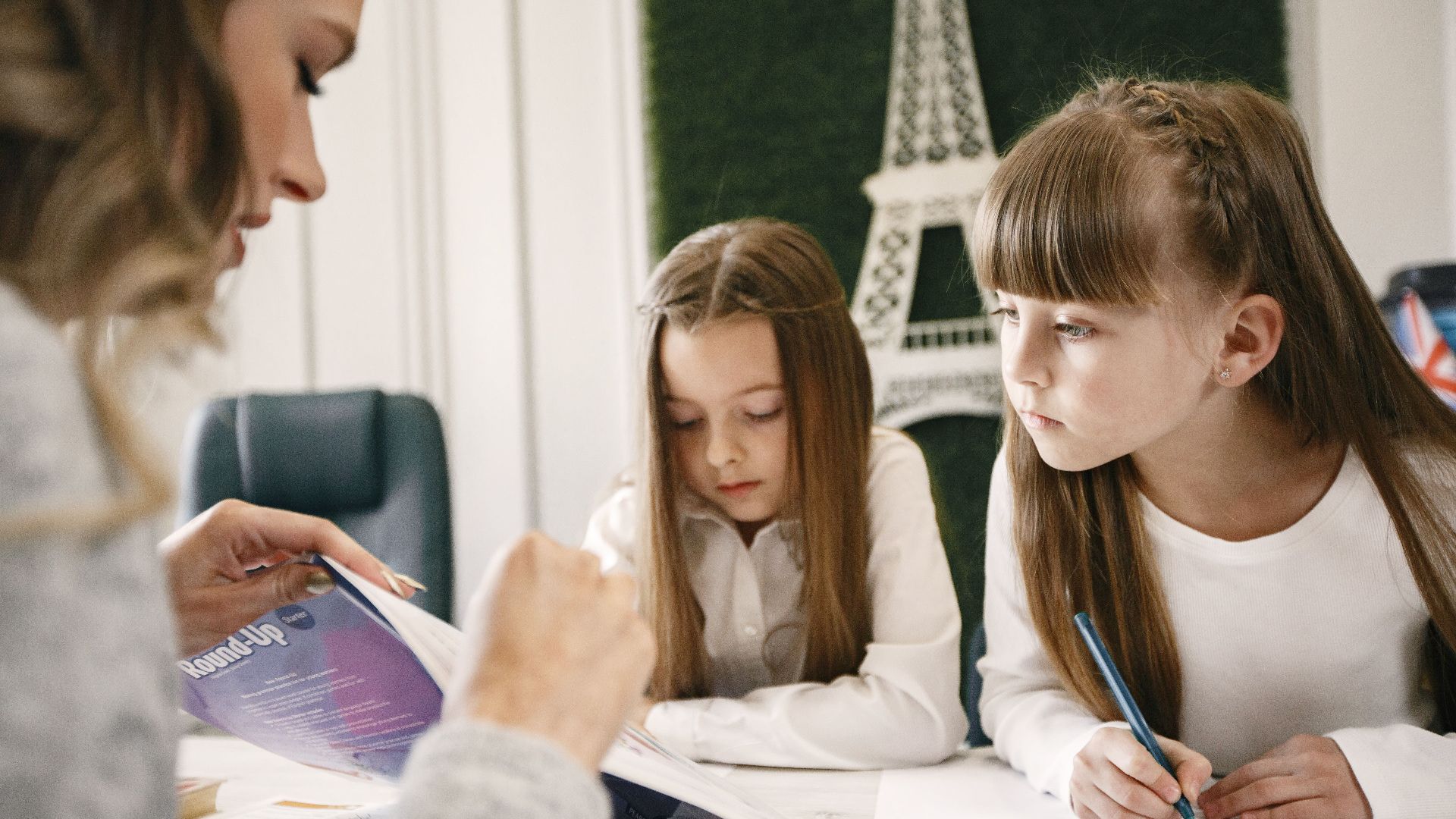 Two girls attentively studying with a tutor in a classroom setting.
