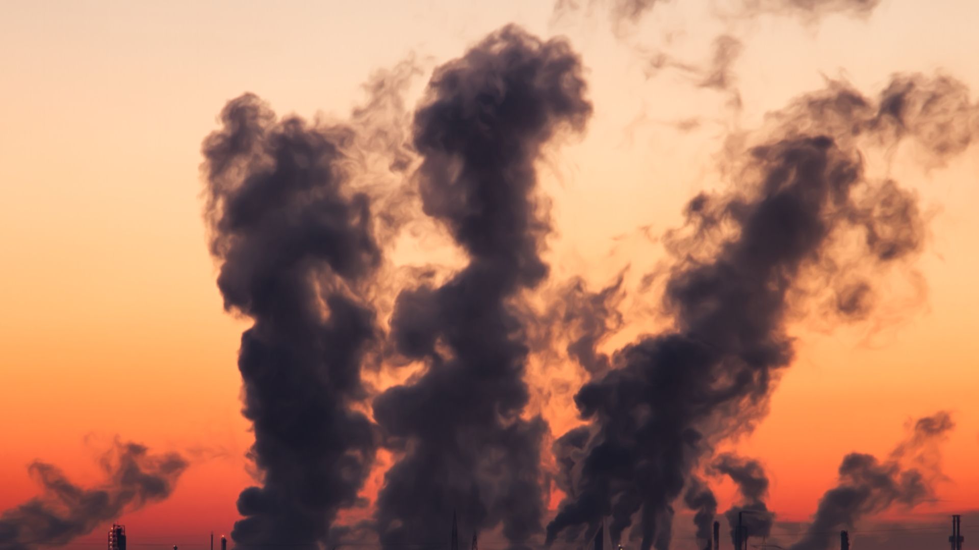 Silhouette of a factory with smoke emissions against a vibrant sunset sky.
