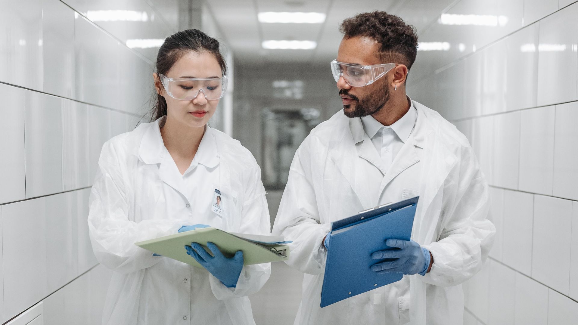 Two scientists in lab coats discussing research documents in a laboratory hallway.