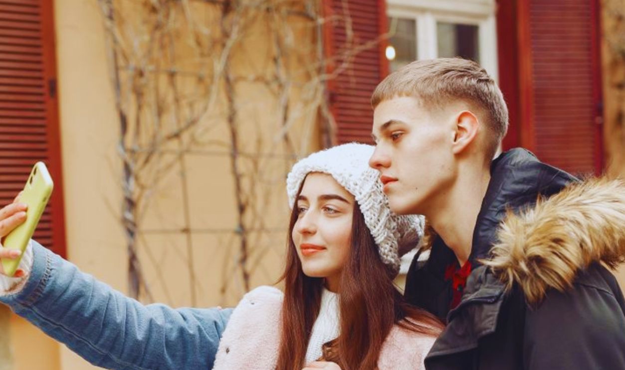 A young couple takes a selfie outdoors, enjoying a winter day together in a cozy setting