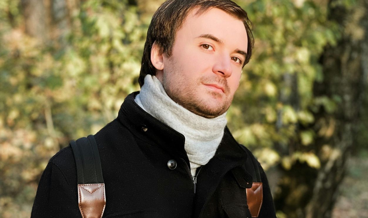 Portrait of a young man wearing a black coat, surrounded by autumn foliage in Russia.