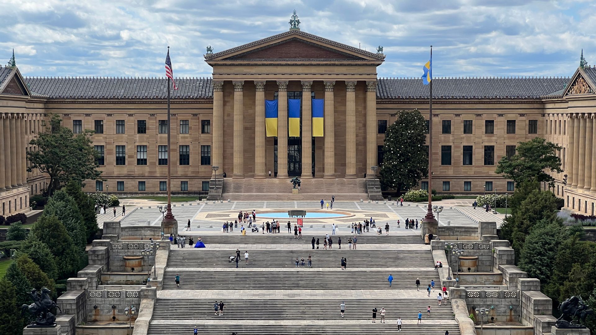 Main building of the Philadelphia Museum of Art, with banners of the Ukrainian flag.  Taken on June 18th, 2022 from the top of the carousel in The Oval XP, an eight-acre warm-weather urban oasis on the Benjamin Franklin Parkway.