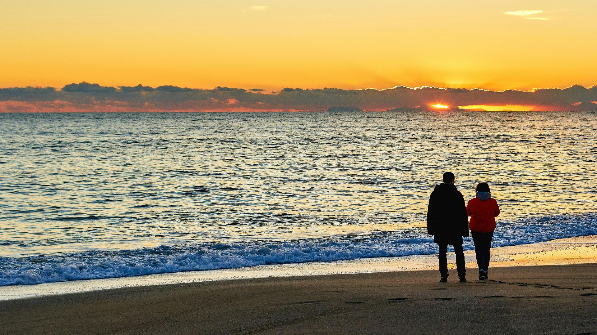 A couple walks along a serene beach at sunset, admiring the golden horizon.