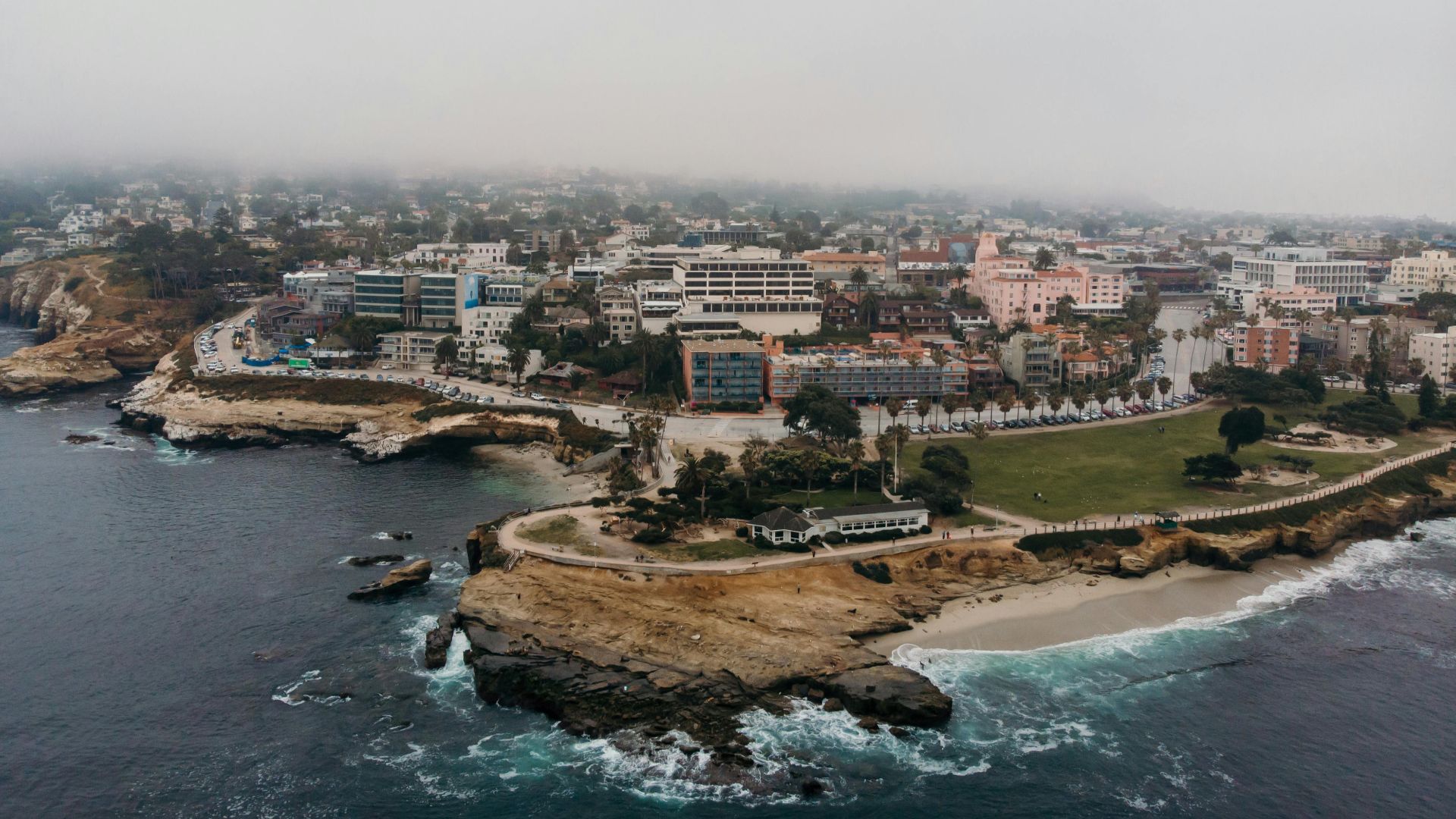 Aerial shot of La Jolla Cove in San Diego, California, showcasing coastal cliffs, cityscape, and foggy atmosphere.