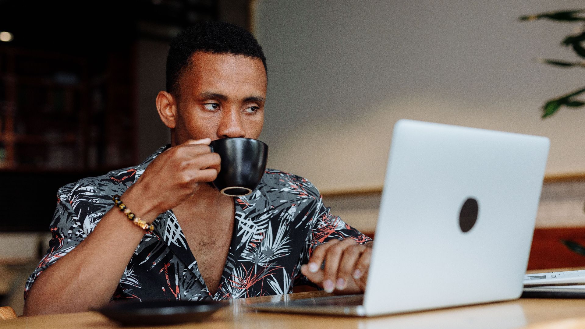 A man sipping coffee while working on a laptop in a cozy cafe.