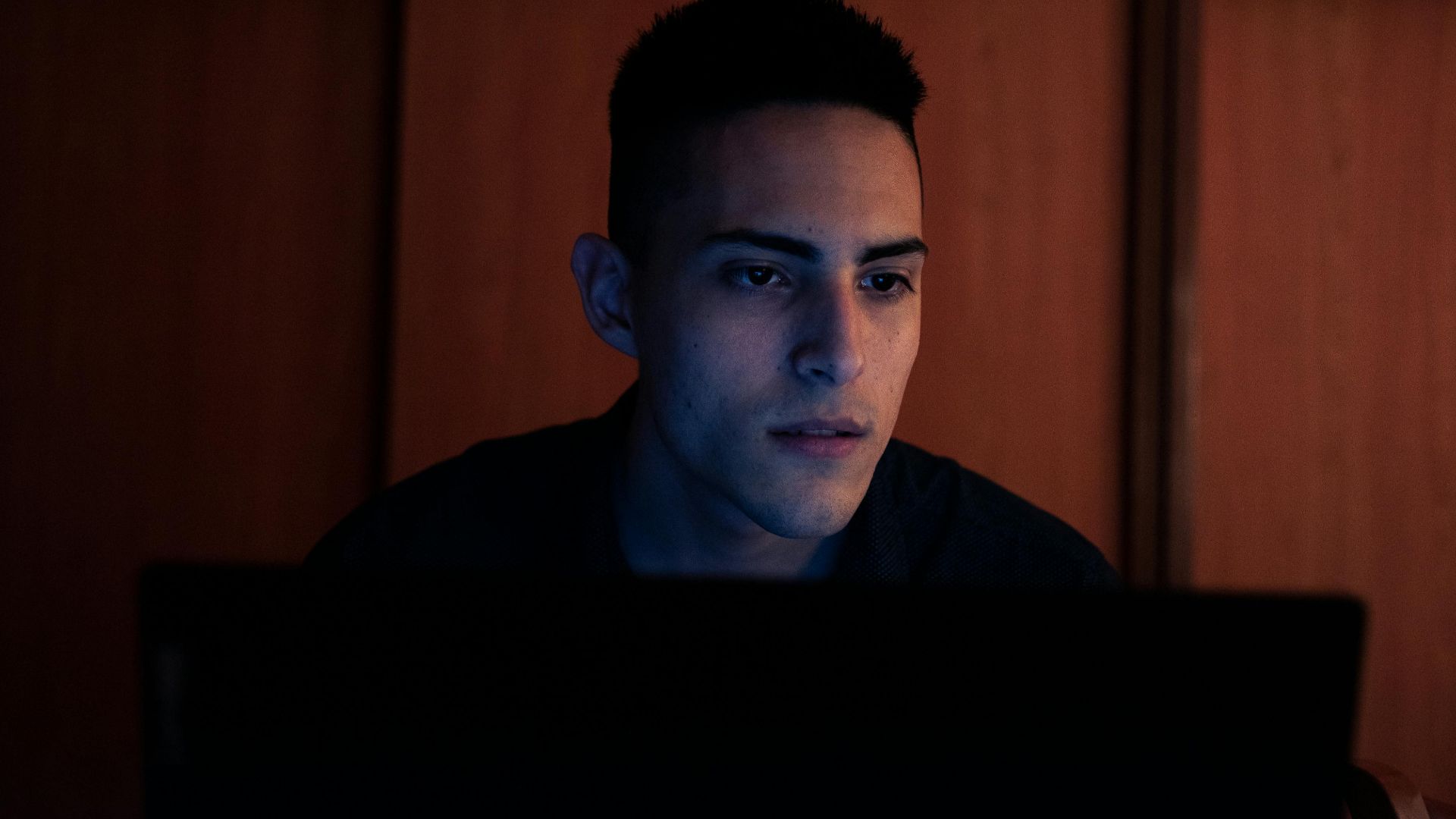 Young man working on a laptop indoors at night in Buenos Aires, capturing focus and concentration.
