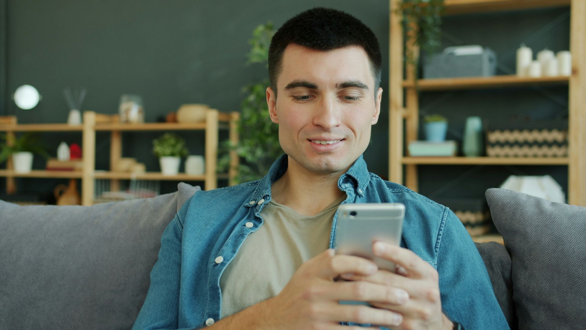 Man smiling while holding a smartphone on a couch.