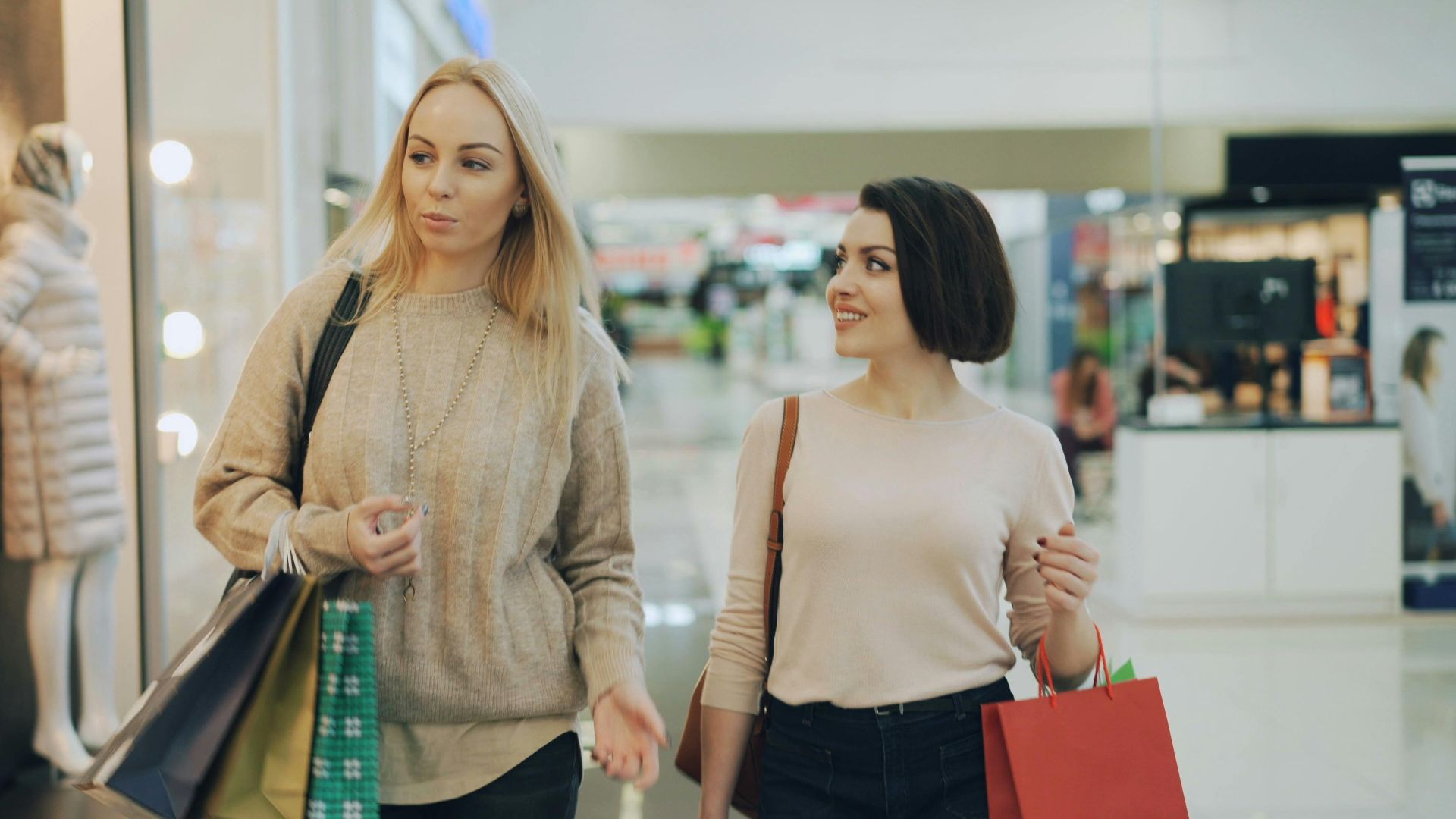 Two women shopping in a mall, carrying bags and enjoying leisure time.
