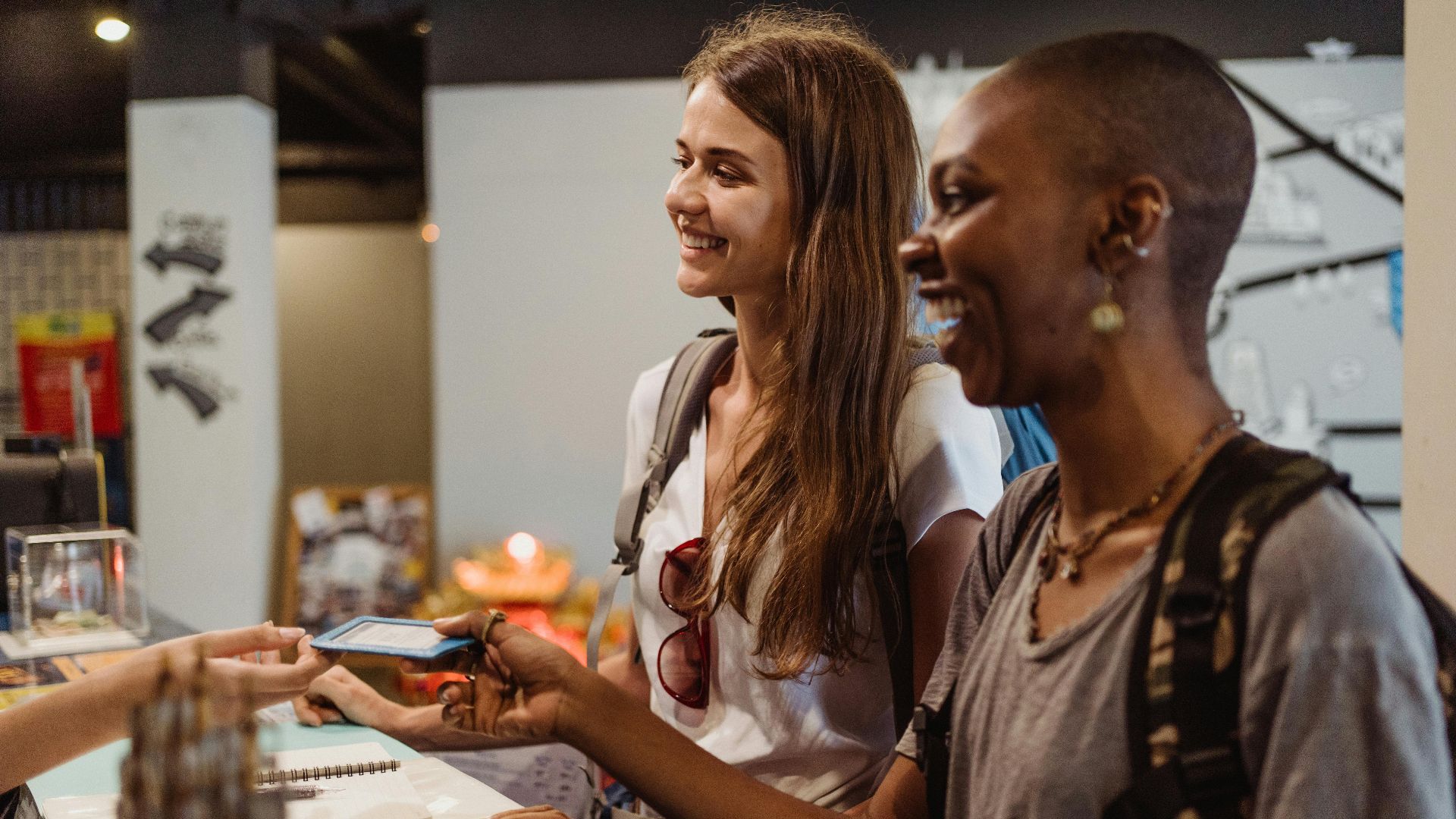 Two women enjoying a cheerful check-in at a hostel reception desk.