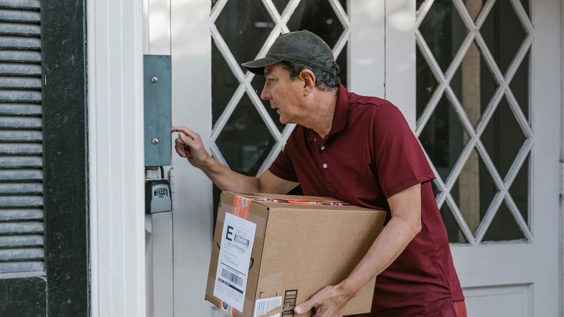 Man delivering a package at a front door, wearing a red shirt and cap.