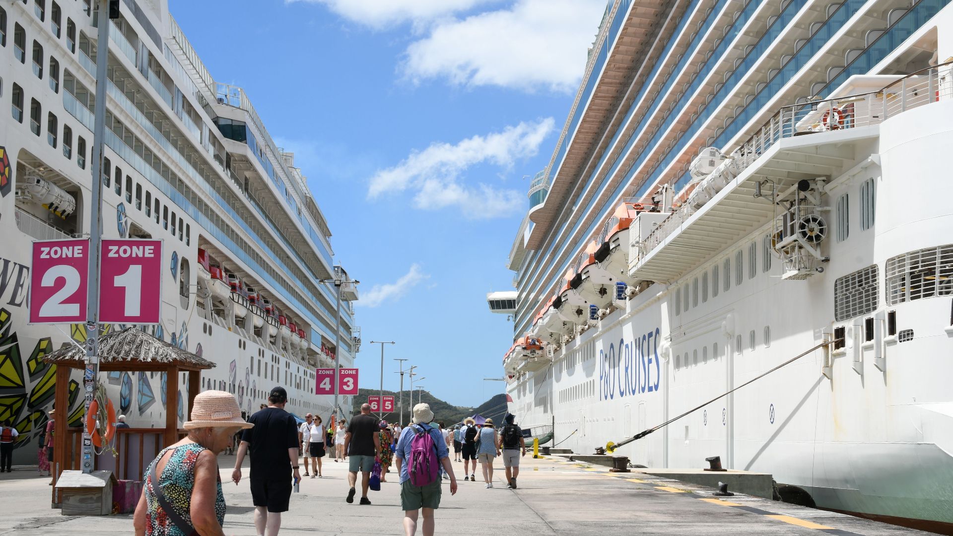 Bustling cruise port with tourists, featuring two large cruise ships under a bright blue sky.