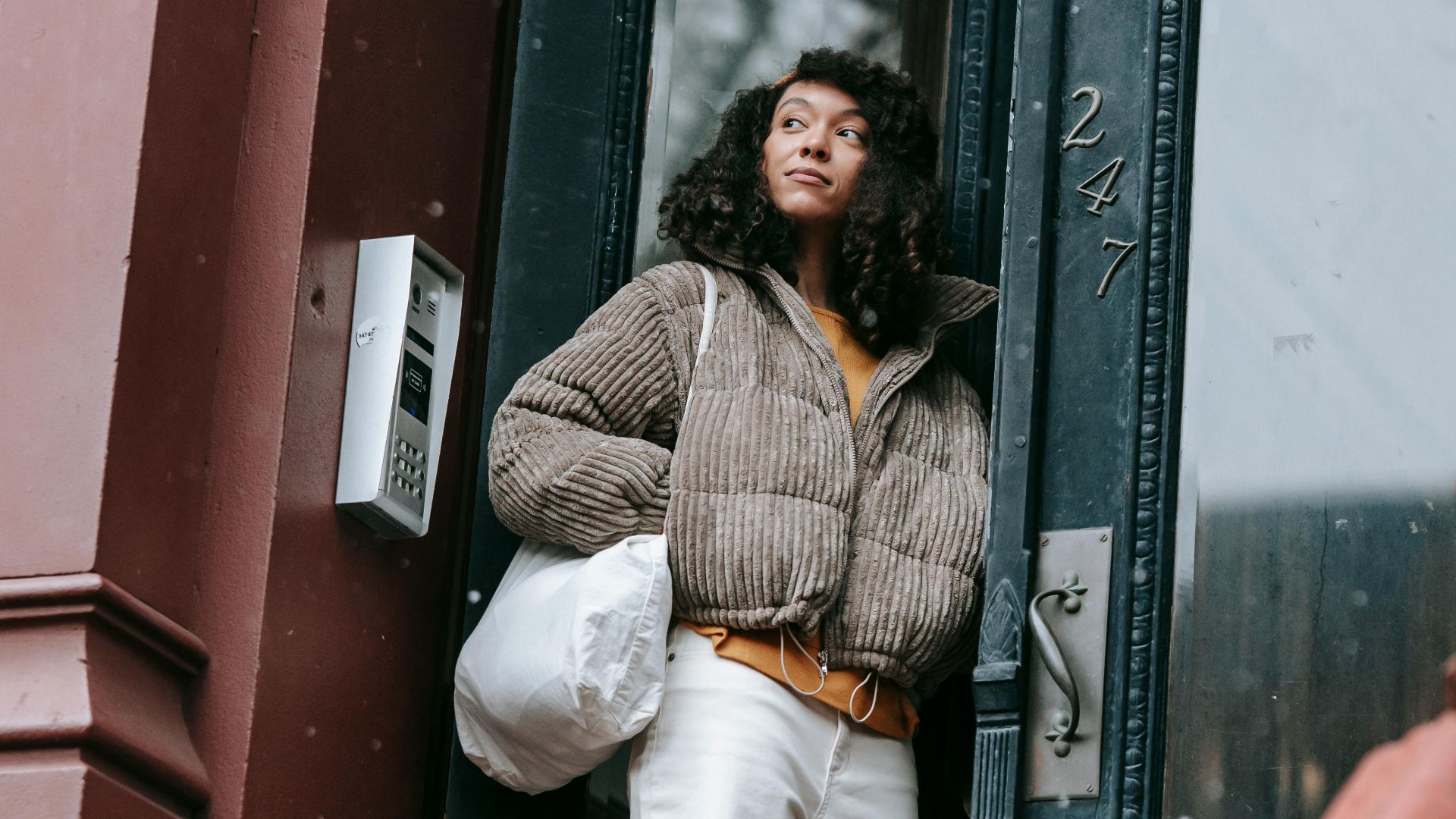 Stylish young ethnic female with hands in pockets looking away in house door in town