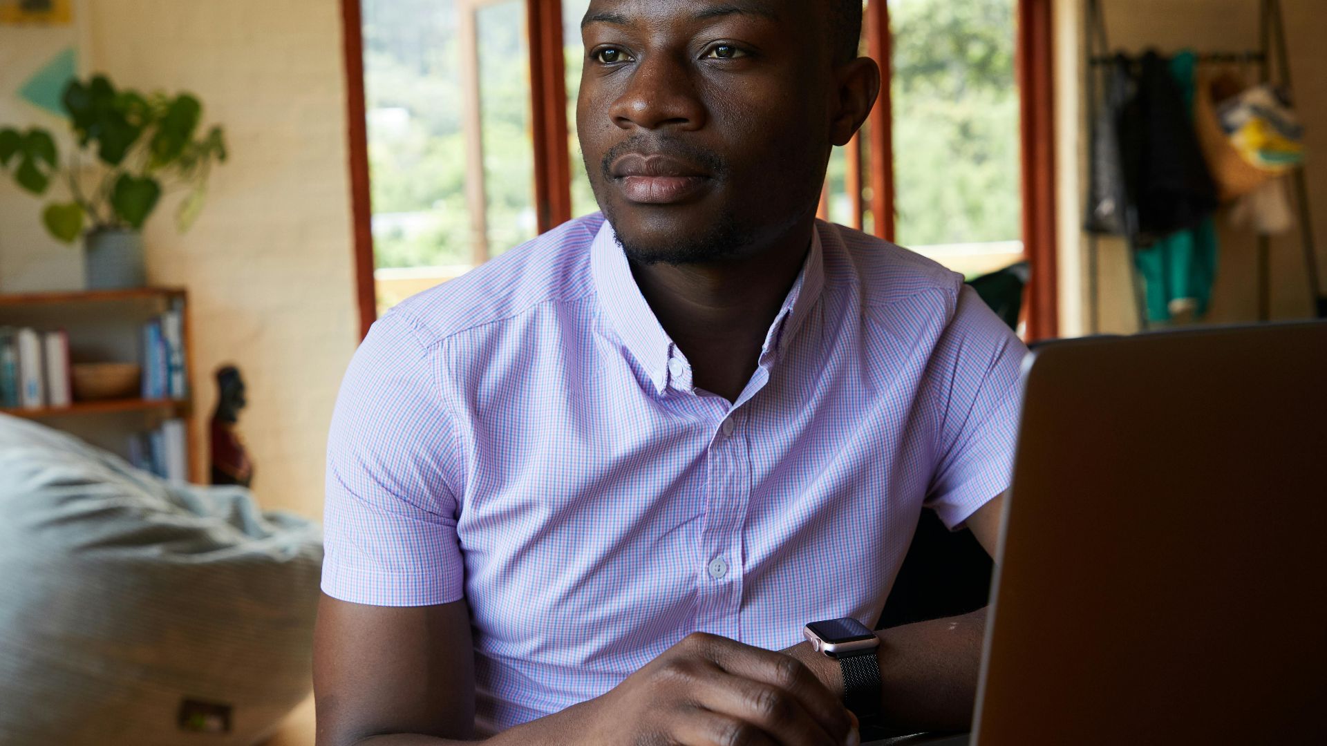 Content young African American male businessman in shirt looking away while using netbook and working remotely in lounge