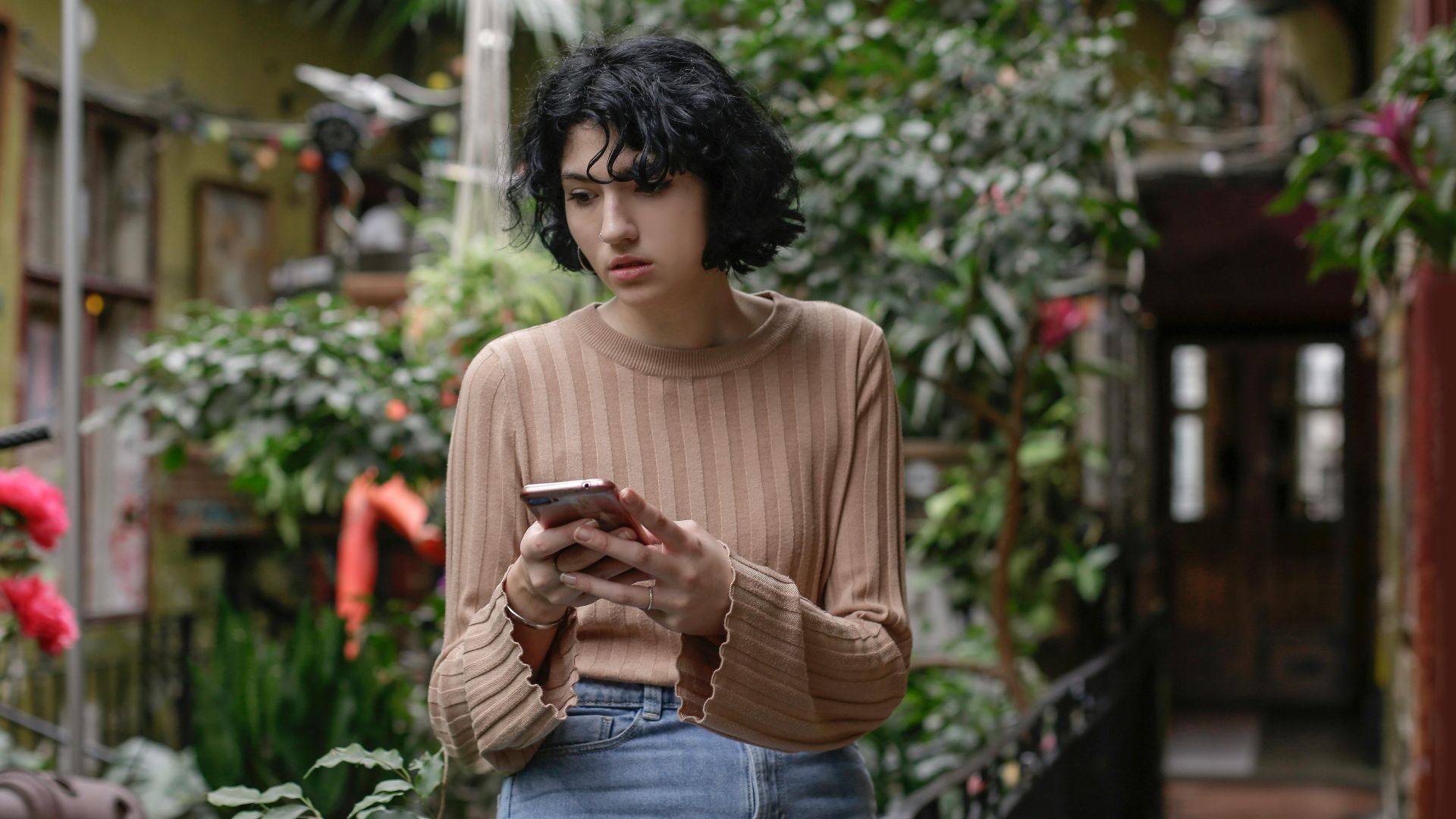 A young woman browsing her smartphone in a lush indoor garden with vibrant greenery.