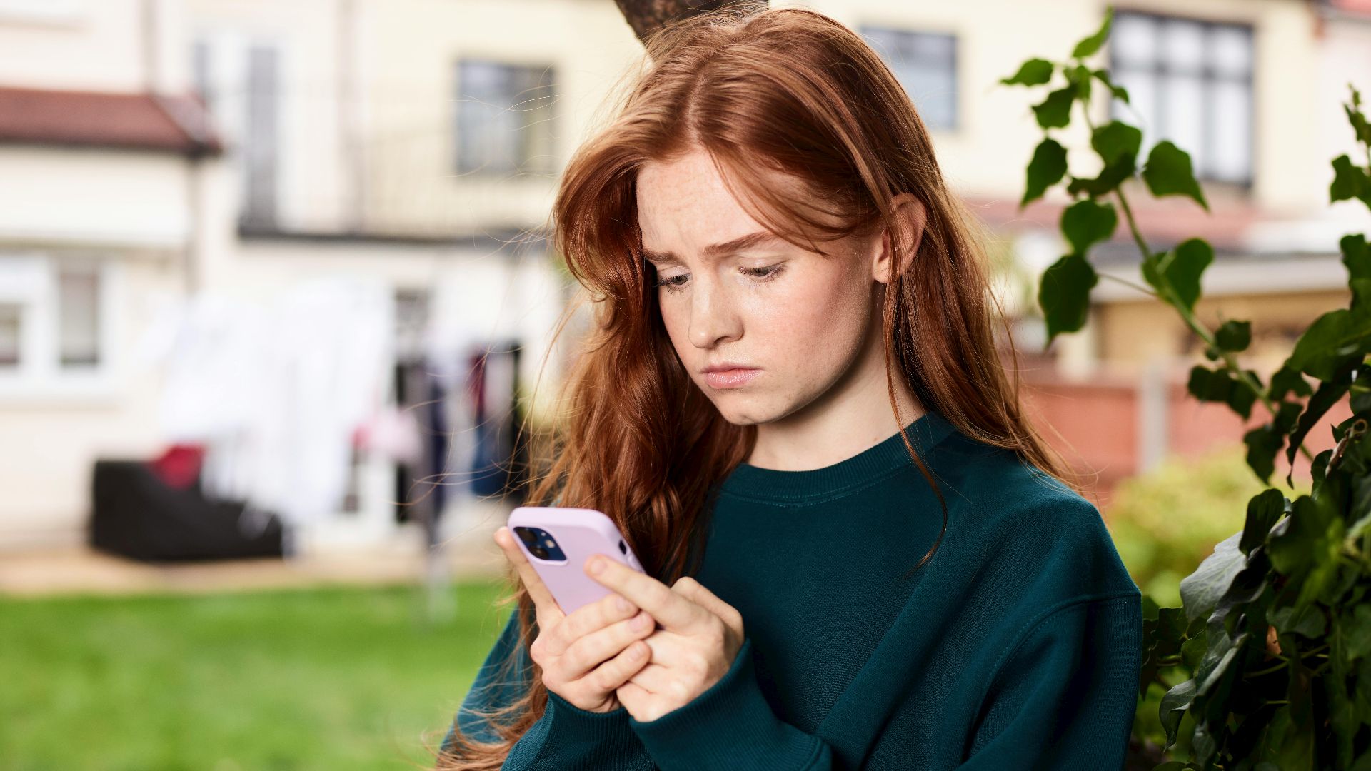 Teen girl with red hair looking at phone outdoors in a courtyard.