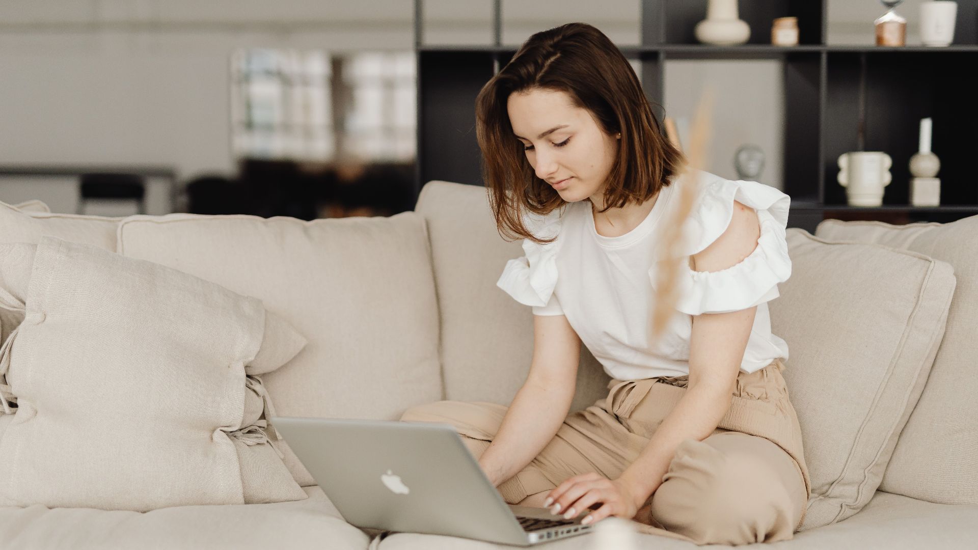 A woman sits on a comfortable couch working on a laptop in a cozy home setting.