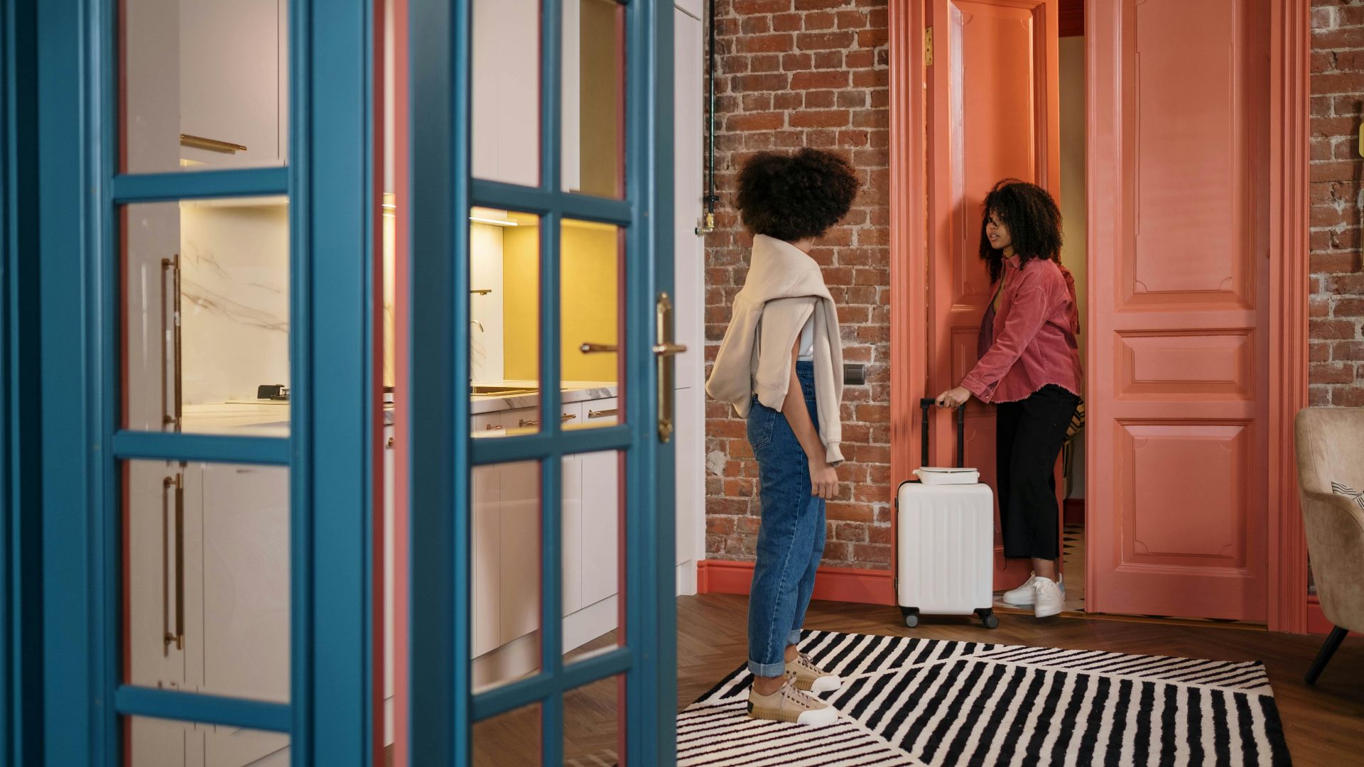 Two women with luggage in a stylish apartment hallway, getting ready to travel.