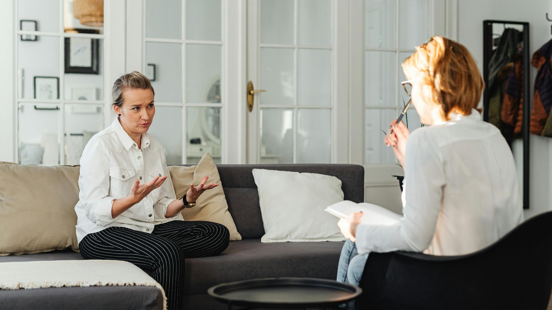 A counseling session taking place in a modern living room with two women engaged in conversation.
