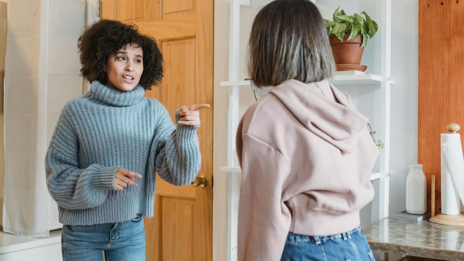 Angry African American female complaining and pointing at faceless female while having fight i modern flat with green plants