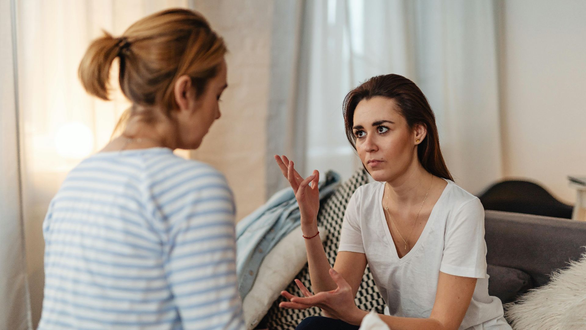 Two women sitting on a sofa, engaged in a serious discussion at home.
