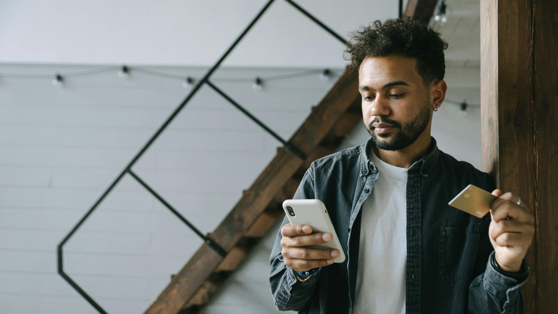 A young man using a smartphone and credit card for online shopping indoors.