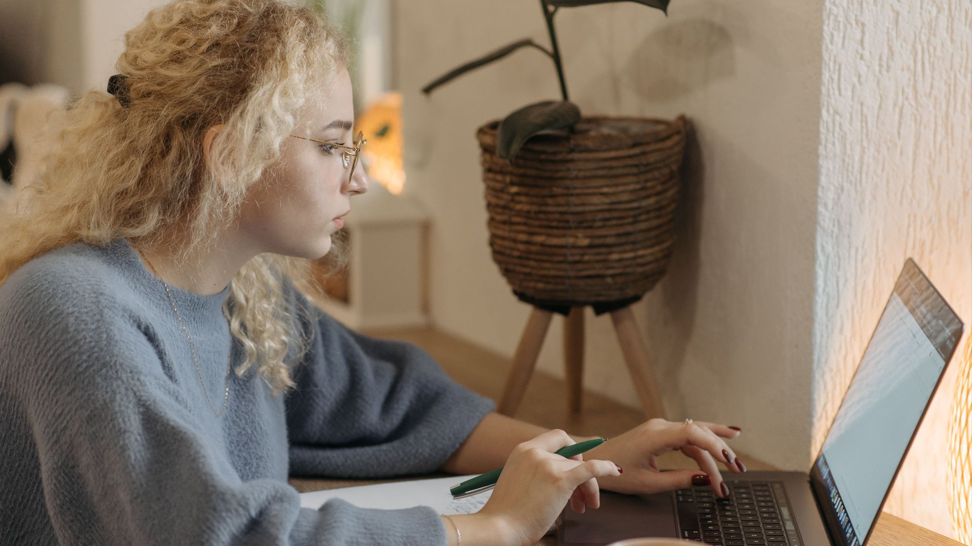 Young woman focused on remote work in a cozy indoor setting with a laptop and coffee cup.