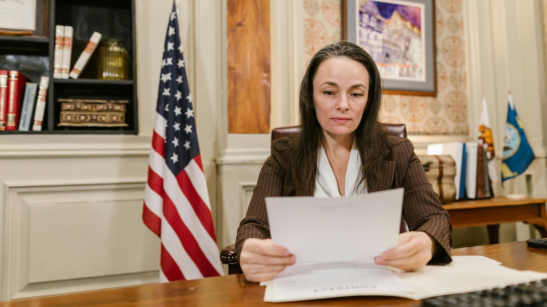 A professional woman reviewing legal documents in an office with flags and books.