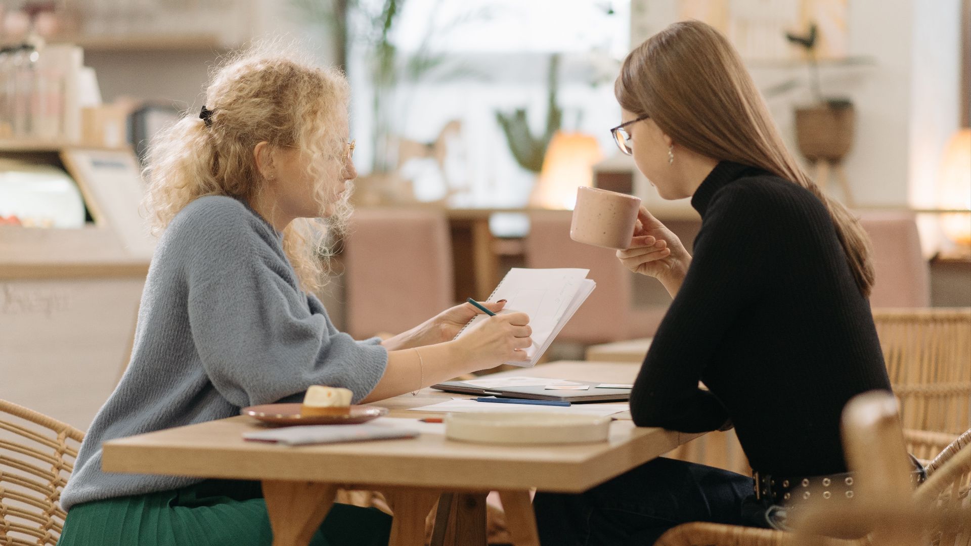 Two women discussing ideas over coffee in a cozy cafe, focused and engaged in conversation.