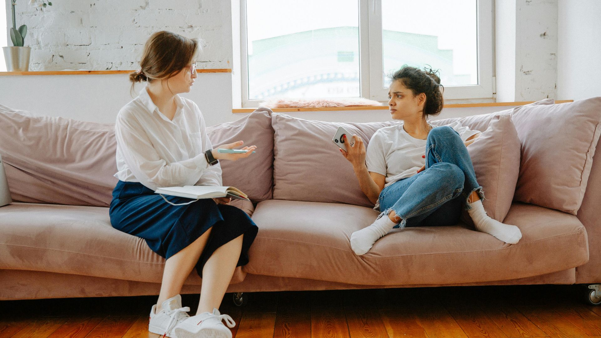 Two women engaging in a therapy session, discussing issues indoors on a couch.