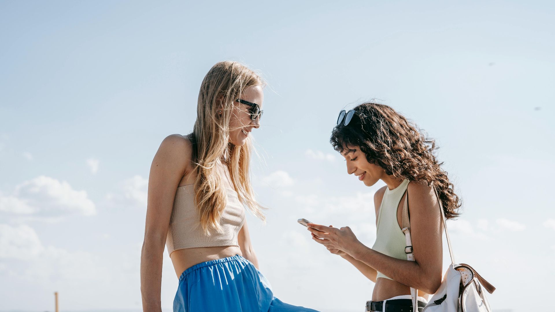 Two young women enjoying the sunny outdoors with smartphones, capturing fun moments.