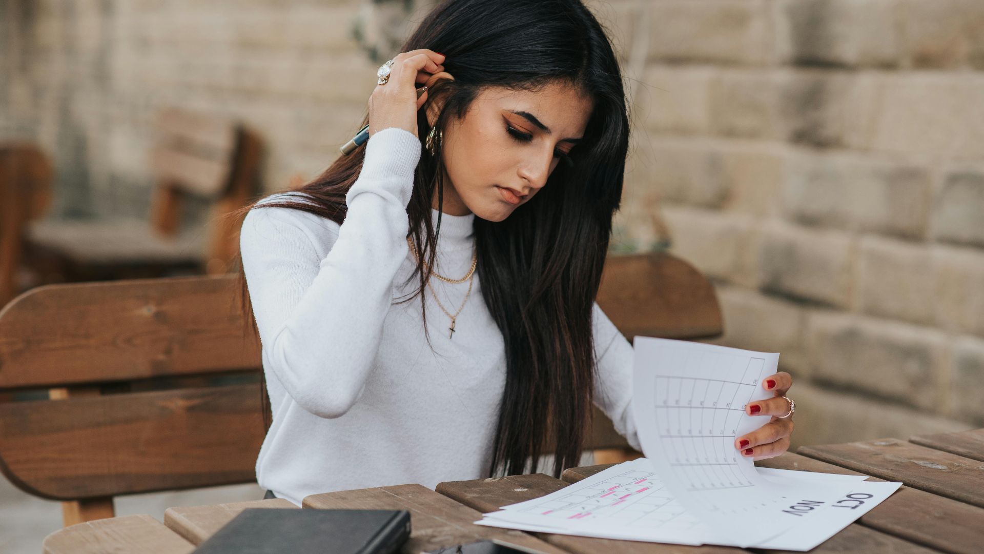 Young ethnic female student in casual outfit with dark hair at wooden table looking through plans in calendar